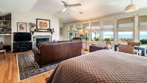 A spacious living room with a fireplace, leather sofa, and large windows offering a view of the ocean. - 9 Bedroom Oceanfront Beach House in Debordieu (Georgetown)