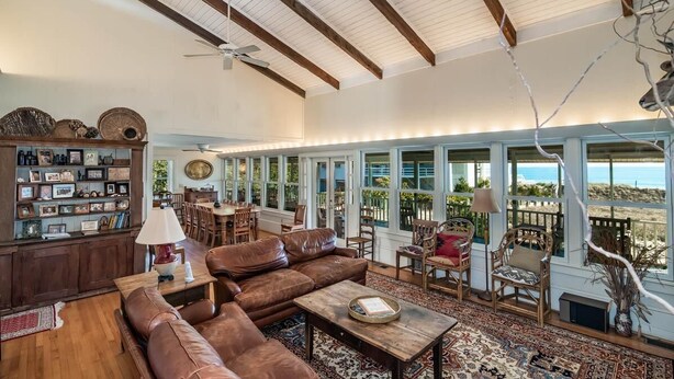 A spacious living room with a large brown leather sofa, wooden coffee table, and a bookshelf filled with books and decorative items. - 9 Bedroom Oceanfront Beach House in Debordieu (Georgetown)