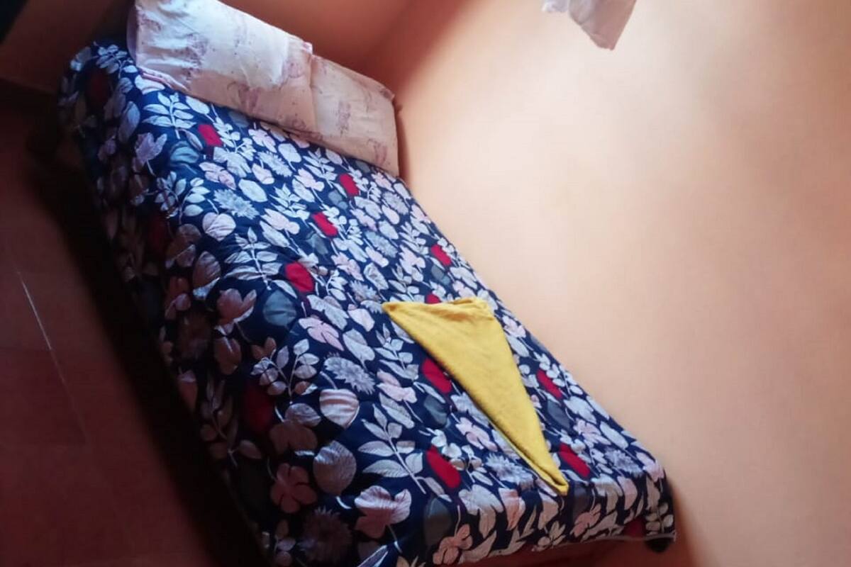 Quarto pequeno com uma cama de solteiro, edredom estampado com flores, um travesseiro amarelo e mosquiteiro.