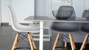 Ein moderner Essbereich mit einem weißen Tisch, zwei Stühlen mit Holzbeinen und einer schwarzen Schüssel auf dem Tisch.