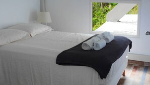 Ein ordentlich bezogenes Bett mit weißen Leinen, einer dunklen Tagesdecke und aufgerollten Handtüchern daneben.