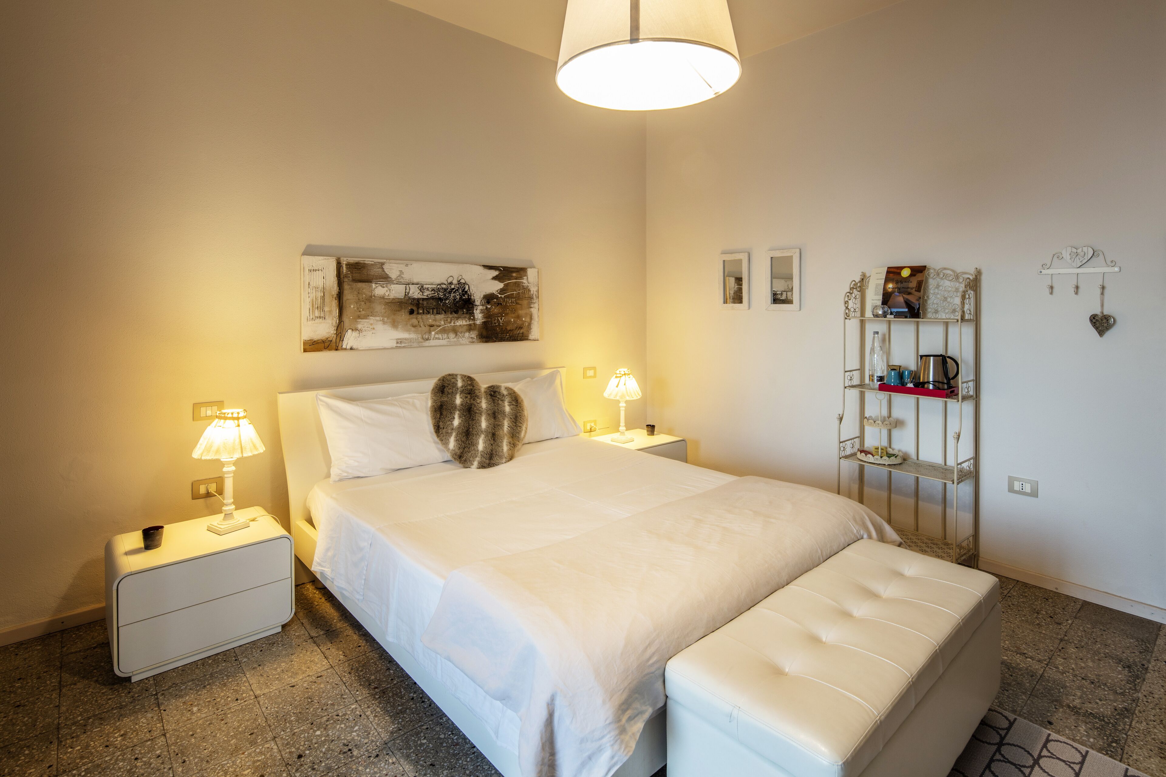 A neatly arranged bedroom with a large bed, bedside lamps, a bedside table, a decorative shelf, and a wall-mounted clock.