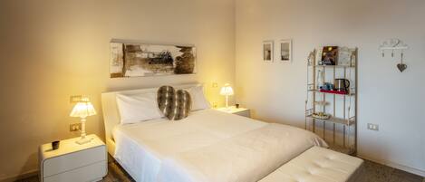 A neatly arranged bedroom with a large bed, bedside lamps, a bedside table, a decorative shelf, and a wall-mounted clock.