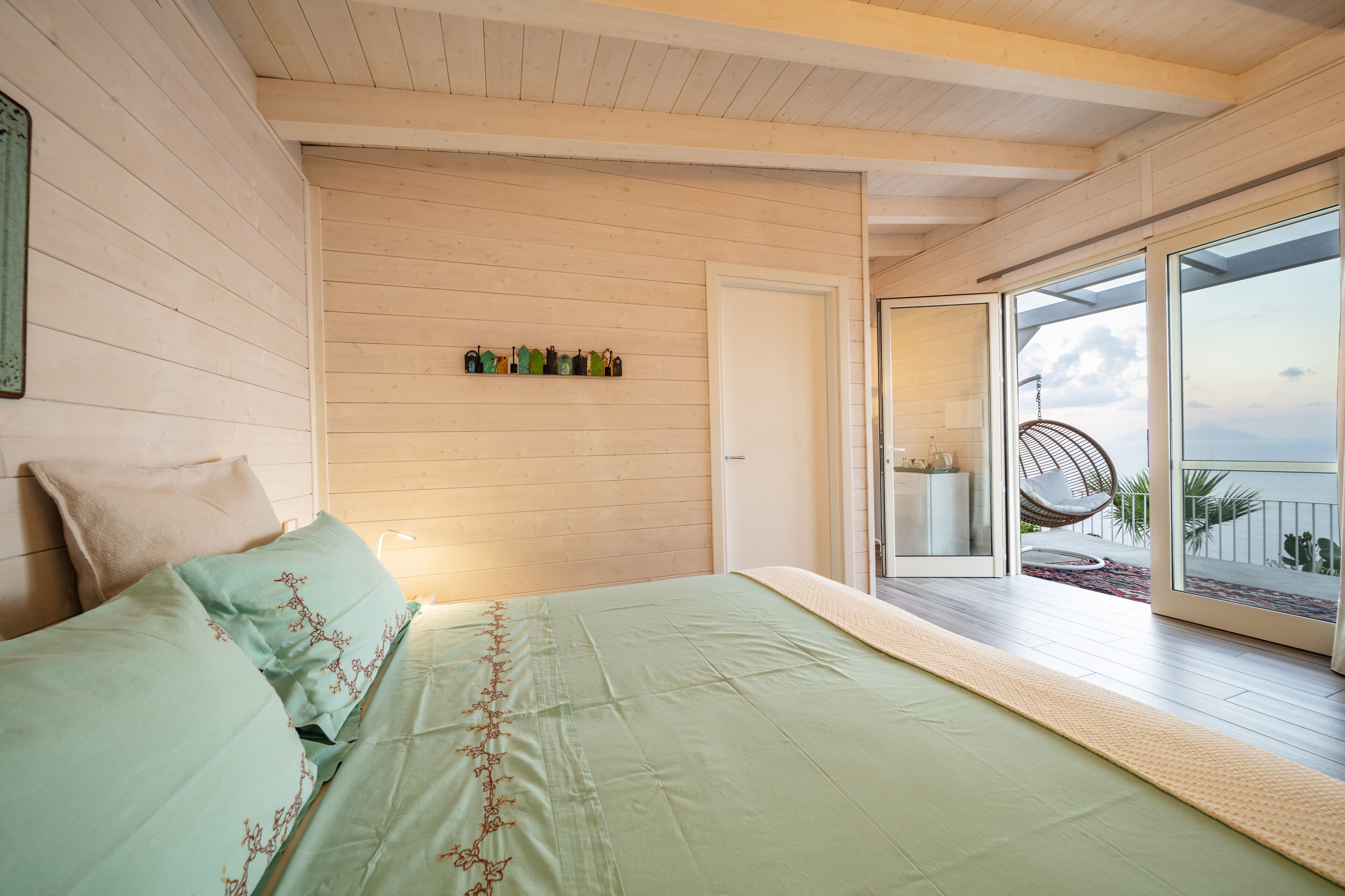 Et soveværelse med en stor seng, en trævæg, en dør til en balkon og udsigt ud.