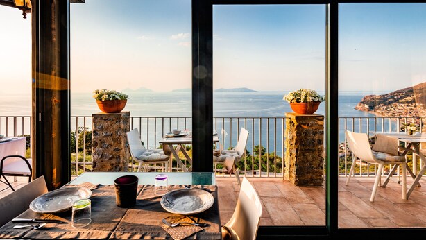 Un coin repas avec une table dressée pour deux personnes, offrant une vue panoramique sur la côte.