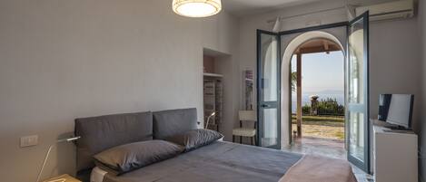 Une chambre à coucher avec un lit, une table de chevet, une lampe et une porte ouverte donnant sur un balcon.
