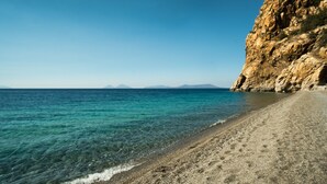 Une plage bordée d’une eau turquoise et limpide, une falaise rocheuse et un rivage de galets.