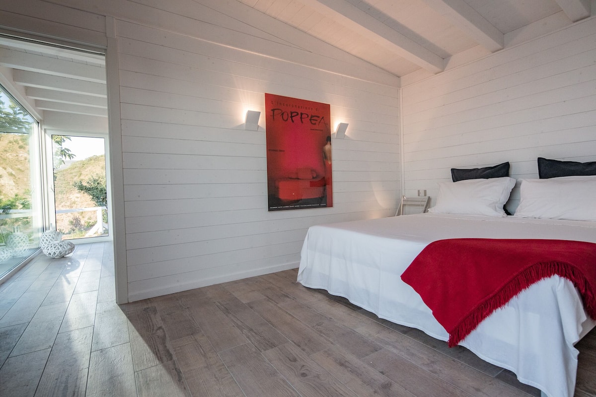 Een slaapkamer met een bed, witte wanden, houten vloer, een poster en een raam.