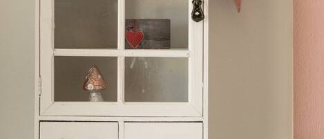 A white cabinet with six glass doors, two drawers at the bottom, and a heart-shaped decoration hanging on the wall to the right.