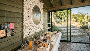 Un buffet de petit-déjeuner proposant une grande variété d’aliments et de boissons, un miroir décoratif et une terrasse dallée de pierre avec vue sur le jardin.