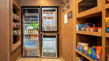 Et hjørne af et hotelværelse med minibar, et køleskab fyldt med drikkevarer og hylder med snacks og diverse.