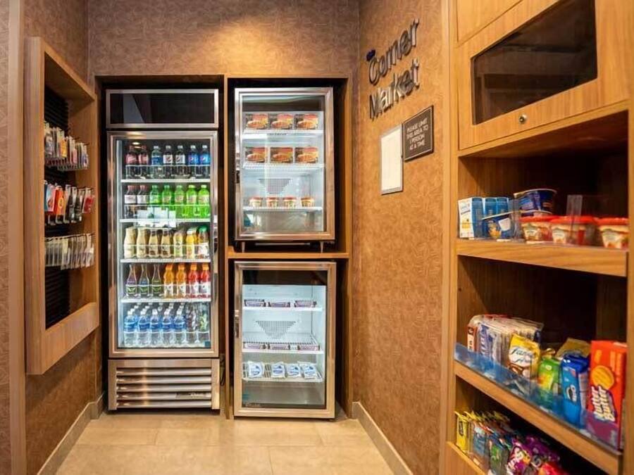 Et hjørne af et hotelværelse med minibar, et køleskab fyldt med drikkevarer og hylder med snacks og diverse.