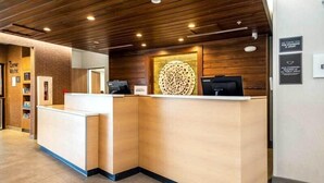 Un espace d’accueil comprenant un comptoir de réception en bois, un élément décoratif fixé au mur et un panneau indiquant que le port du masque est obligatoire.