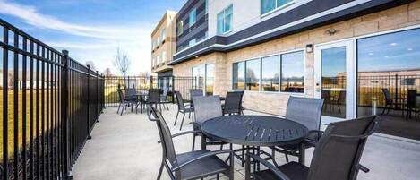 Un patio al aire libre con una mesa redonda y sillas, una cerca de metal negro y un edificio con ventanas grandes y fachada de piedra.