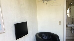 A room with a wooden table, a red and a black chair, a mounted television, and a clothes drying rack. - Motel Hadsten (Hadsten)