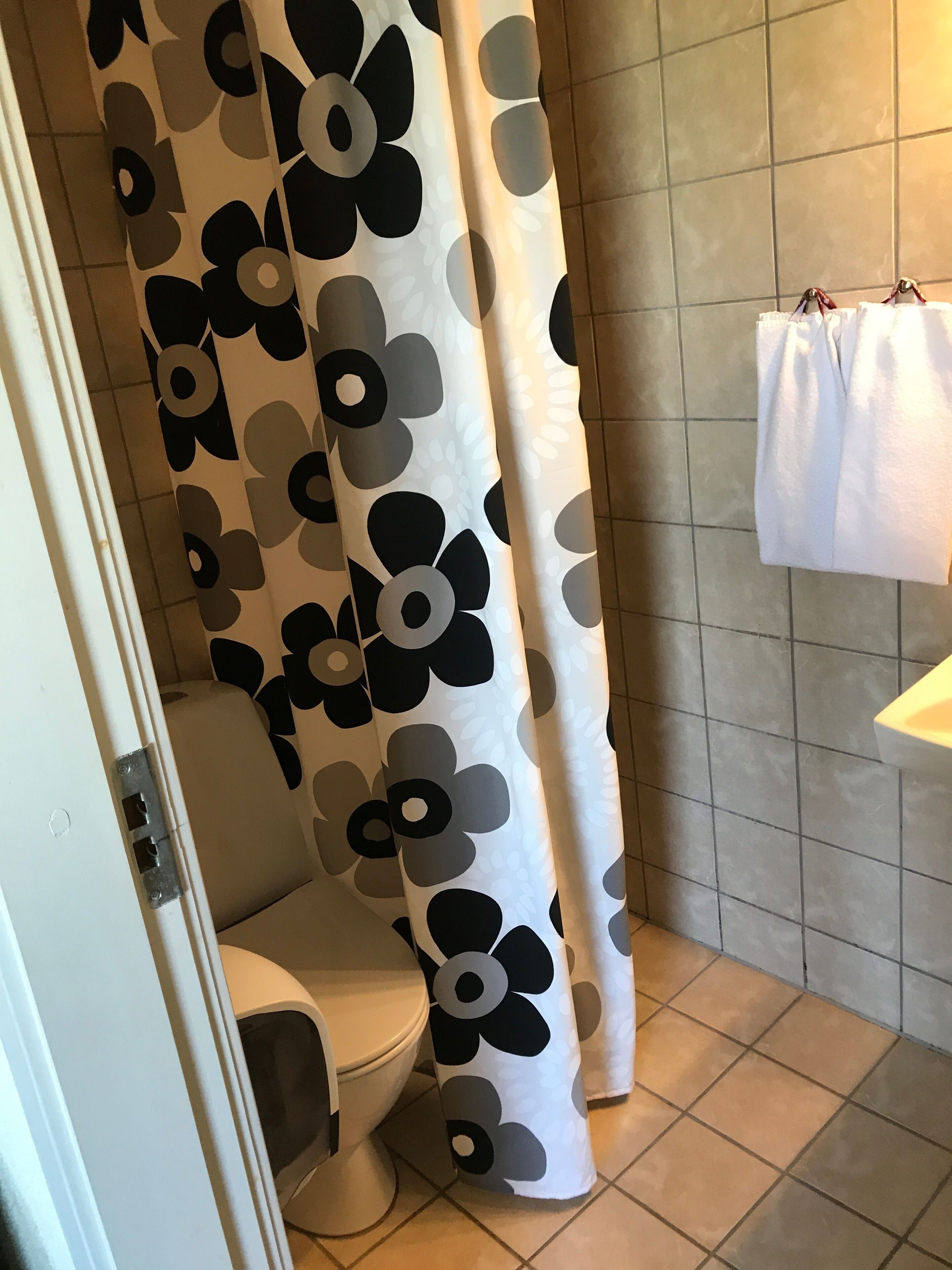Et badeværelse med toilet, bruseforhæng med blomstermønster og et håndklæde på en håndklæderække.