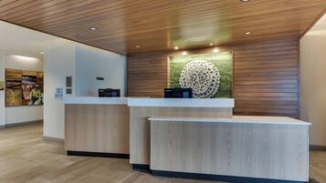A reception area with two light wood reception desks, a wooden ceiling, and a wall-mounted decorative piece.