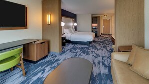 A hotel room with a bed, a desk, a green chair, a sofa, and a TV. - Fairfield Inn & Suites by Marriott Warsaw (Warsaw)