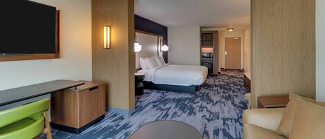 A hotel room with a bed, a desk, a green chair, a sofa, and a TV.