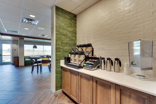 A coffee station with a coffee machine, cups, and thermos. There is a seating area with chairs and a table.