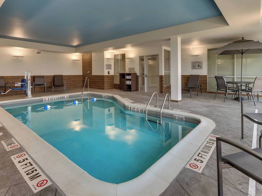 An indoor swimming pool with clear depth markers, a seating area with chairs and tables, and a glass partition wall.