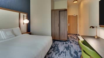 A hotel room with a bed, a desk, a green chair, a wardrobe, and a mirror.