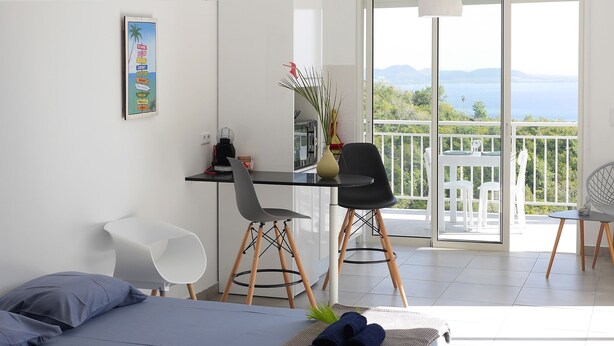 Une chambre à coucher avec un lit, un bureau et des chaises. Elle possède un balcon avec vue sur la mer.