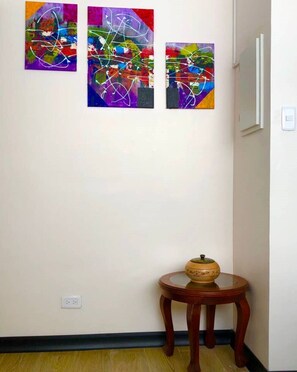 Un couloir orné de trois tableaux abstraits et comprenant une petite table en bois sur laquelle est posé un bol décoratif.