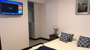 A hotel room with a bed, a nightstand with a lamp, a TV mounted on the wall, and a framed picture on the wall. - Suite location and comfort in Quito Hi speed wifi (Quito)