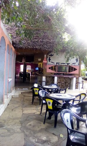 An outdoor seating area with tables and chairs, a Coca-Cola sign, and a TV screen. - Camp David (Makindu)