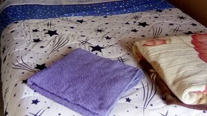 A bed with a star-patterned bedspread, a folded purple towel, and a pink cloth hanging above. - Camp David (Makindu)