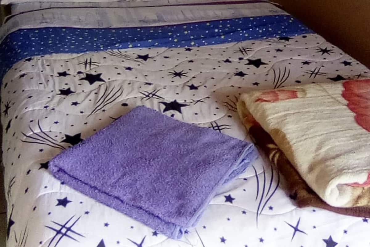 Un lit avec une couvre-lit à motifs étoilés, une serviette violette pliée et un tissu rose suspendu au-dessus.