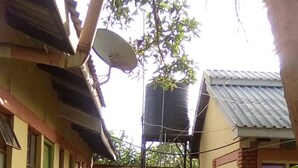 A narrow outdoor corridor with tiled flooring, potted plants, and a water tank. - Camp David (Makindu)