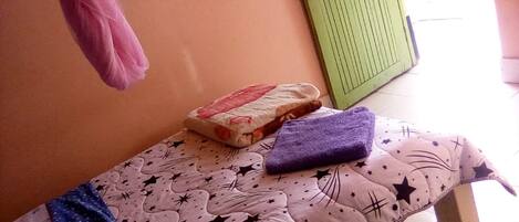 A small room with a bed covered in a star-patterned bedspread, a purple towel, and a pink garment hanging on a hook.
