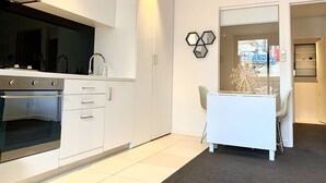 A modern kitchen with white cabinetry, a built-in oven, and a dining area with a white table and chair.