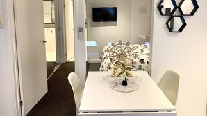 A modern hotel room with a white bed, a TV, a clock, and a unique hexagonal mirror on the wall.