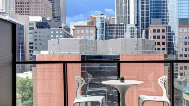 A balcony with two white chairs and a small table, overlooking a cityscape with modern buildings.