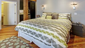 Une chambre à coucher avec un grand lit, des poutres en bois, une porte donnant sur une salle de bain et une table de chevet avec une lampe.