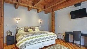 Une chambre à coucher comprenant un lit, des tables de chevet, un bureau, une chaise, un téléviseur et un plafond en bois.