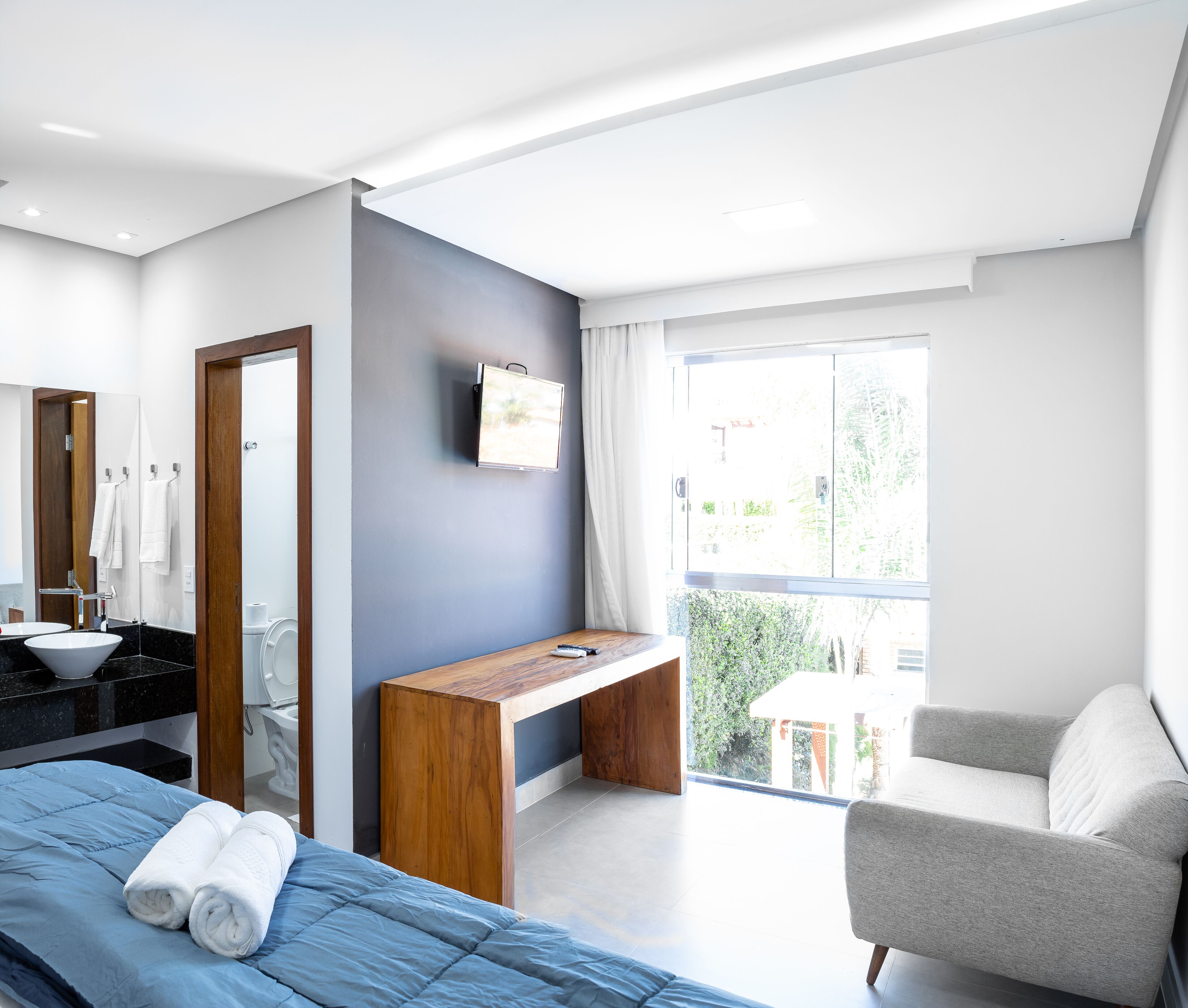 A modern bedroom with a bed, a desk, a chair, a bathroom, and a balcony.