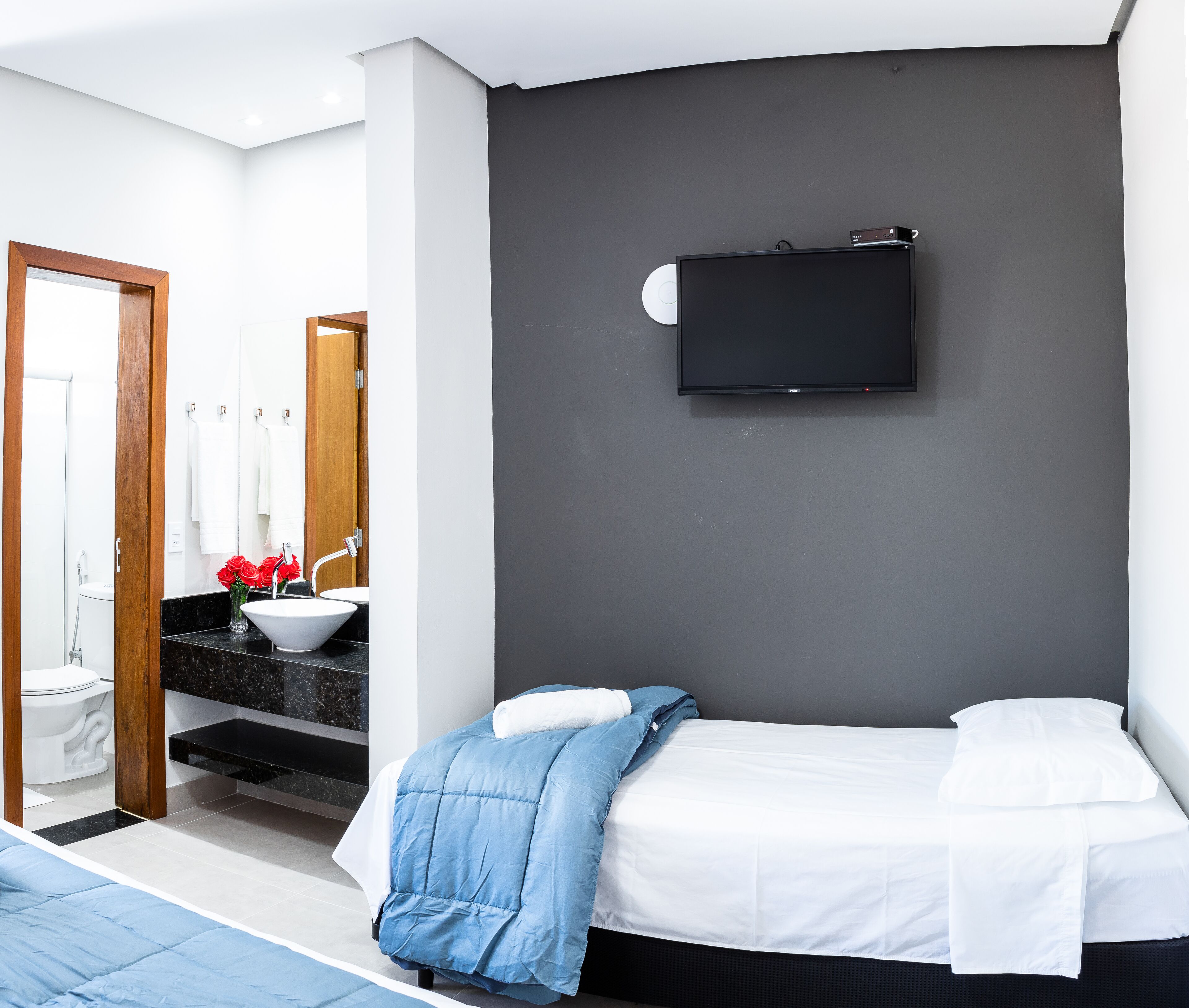 Een moderne hotelkamer met een bed, een aan de muur bevestigde televisie, een badkamer met wastafel en spiegel, en een douchehoek.