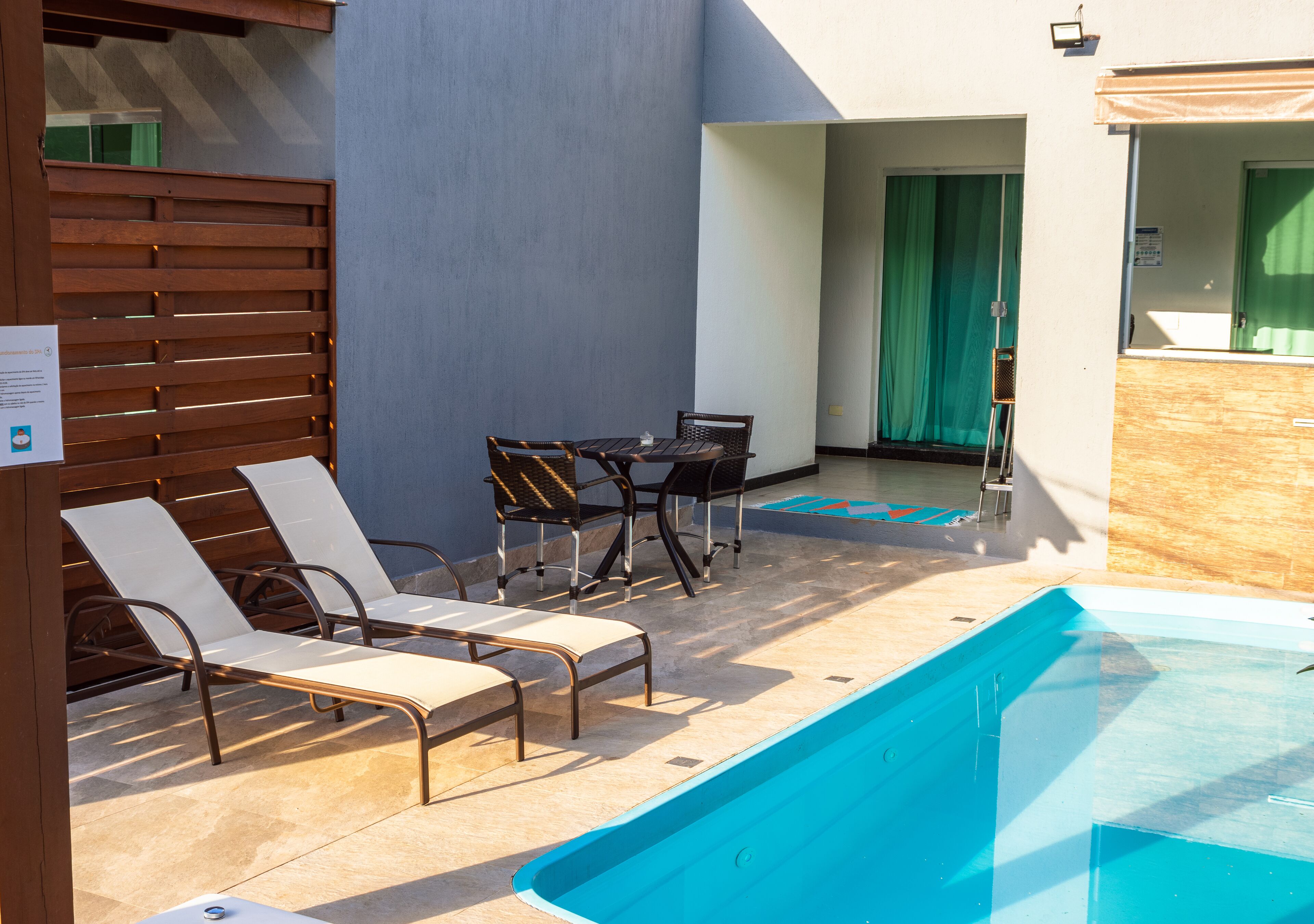Un área de piscina con sillones de descanso y una mesa, una valla de madera y una cortina verde.