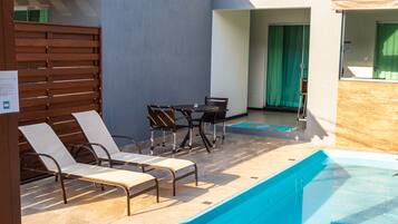Un área de piscina con sillones de descanso y una mesa, una valla de madera y una cortina verde.