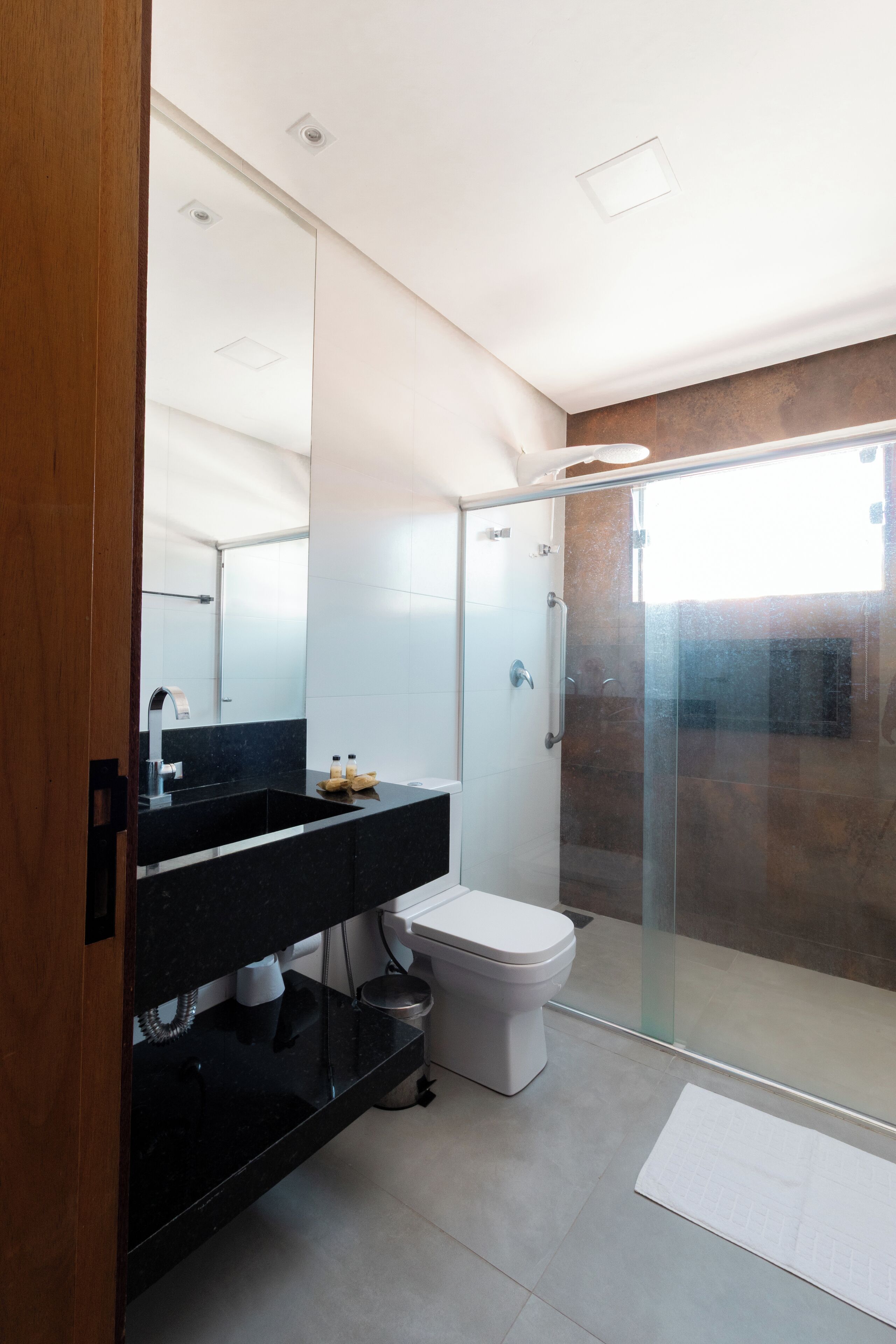 Un baño moderno con encimera negra, inodoro blanco y ducha con mampara de vidrio.