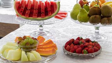 Een tafel met diverse fruitschaaltjes, waaronder watermeloen, peren, kippenfruit, druiven, papaja en aardbeien.