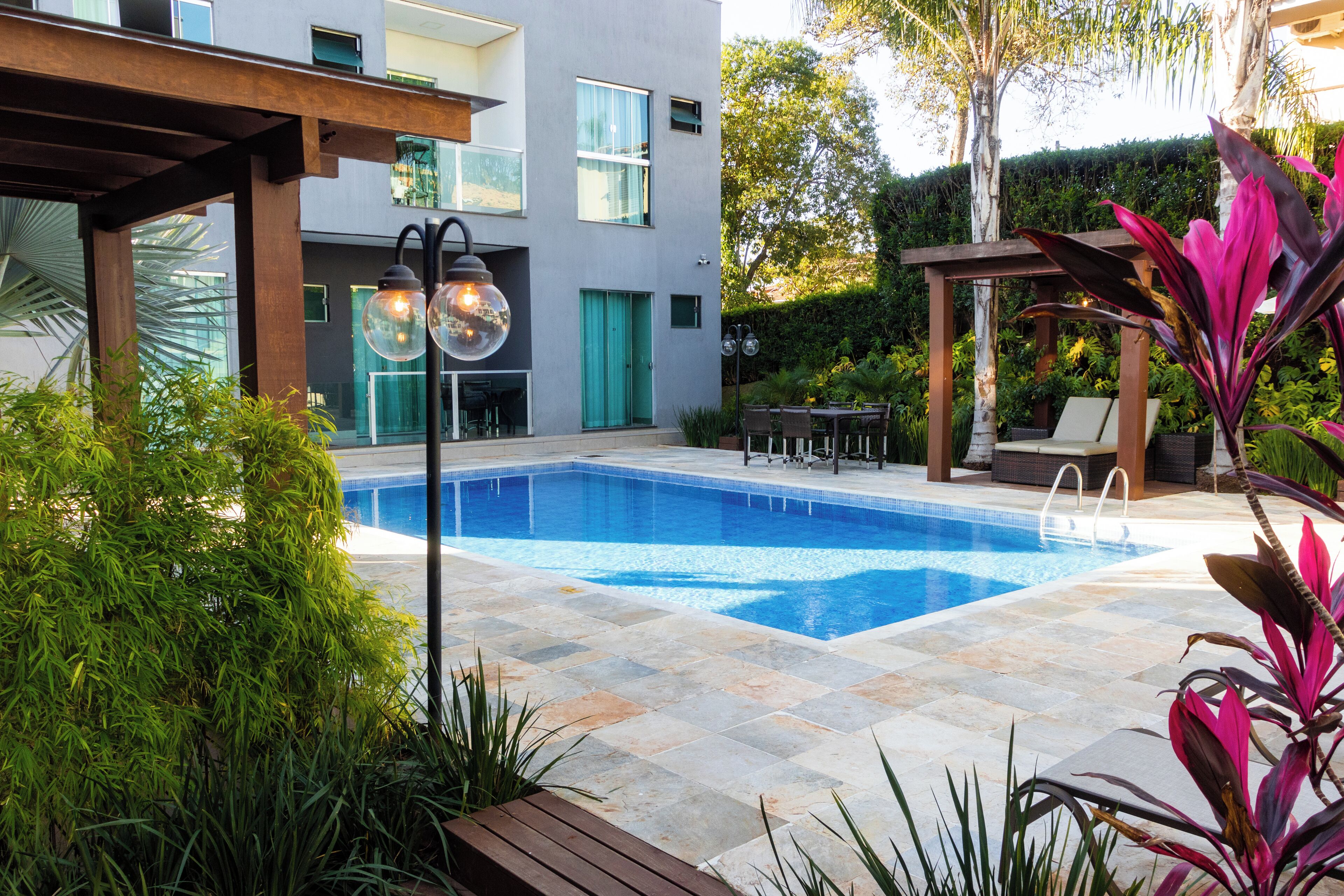 Una piscina con borde de baldosas, rodeada de vegetación y una pérgola.