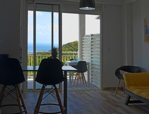 Una habitación con una mesa, sillas, un sofá amarillo y vista al mar a través de amplios ventanales.
