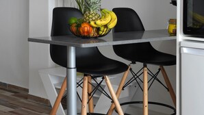 Et moderne køkken med spisebord, to stole, skål med frugt, fjernsyn og køleskab.