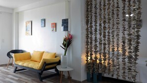 En moderne stue med en gul sofa, et lille hvidt bord og en dekorativ væg med ophængte objekter.