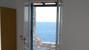 Ett rum med en säng, en dörr som leder ut till en balkong med utsikt över havet och ett klinkergolv.
